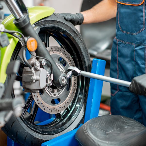 Mechanic tightening motorcycle wheel with a hand wrench during a repairment at the workshop, close-up view